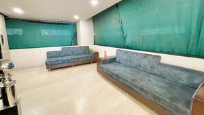 Una habitación con dos sofás grises, una pequeña mesa y una pantalla verde en la pared.