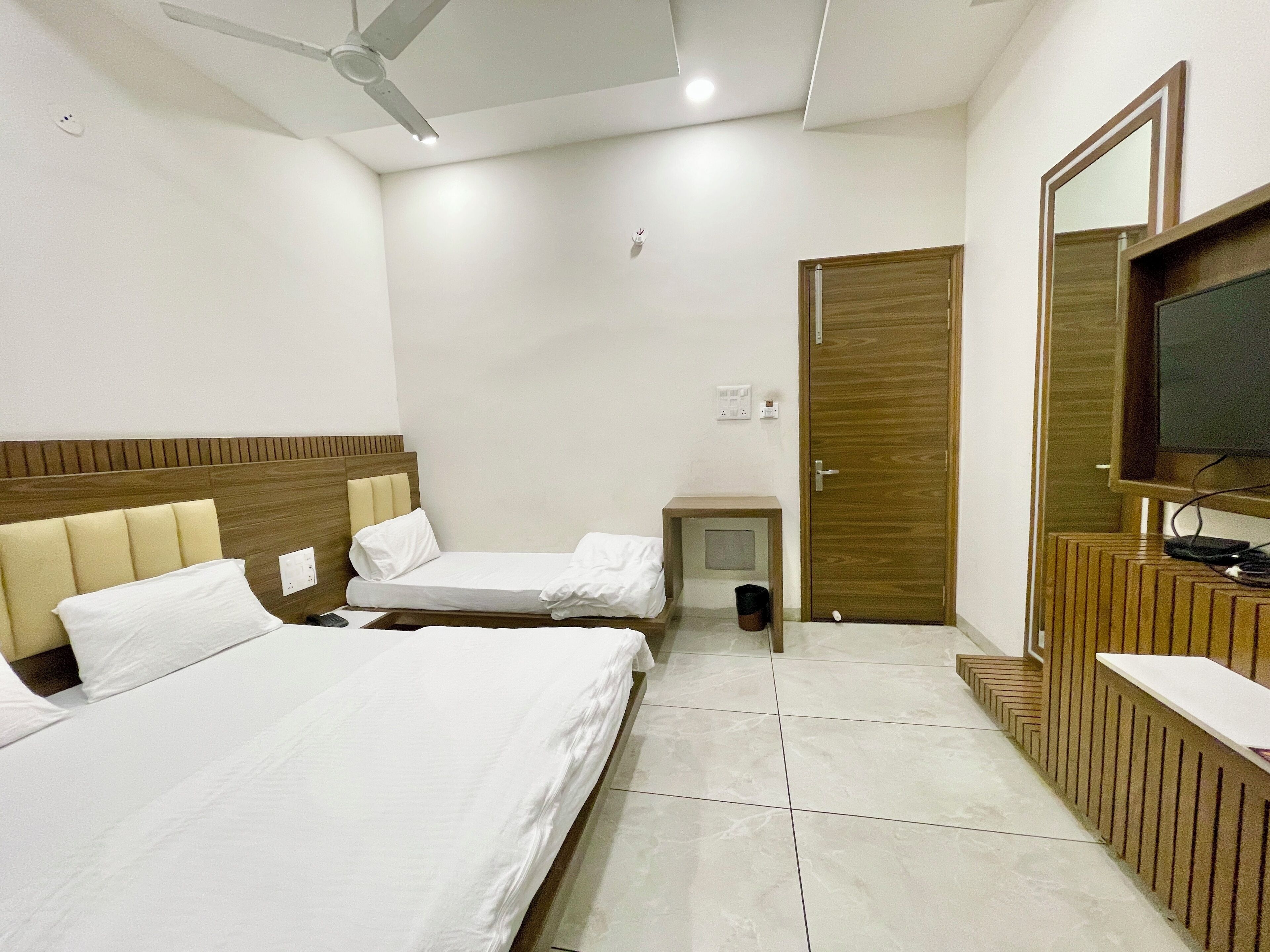 A hotel room with two beds, a TV, a ceiling fan, and a wooden cabinet.