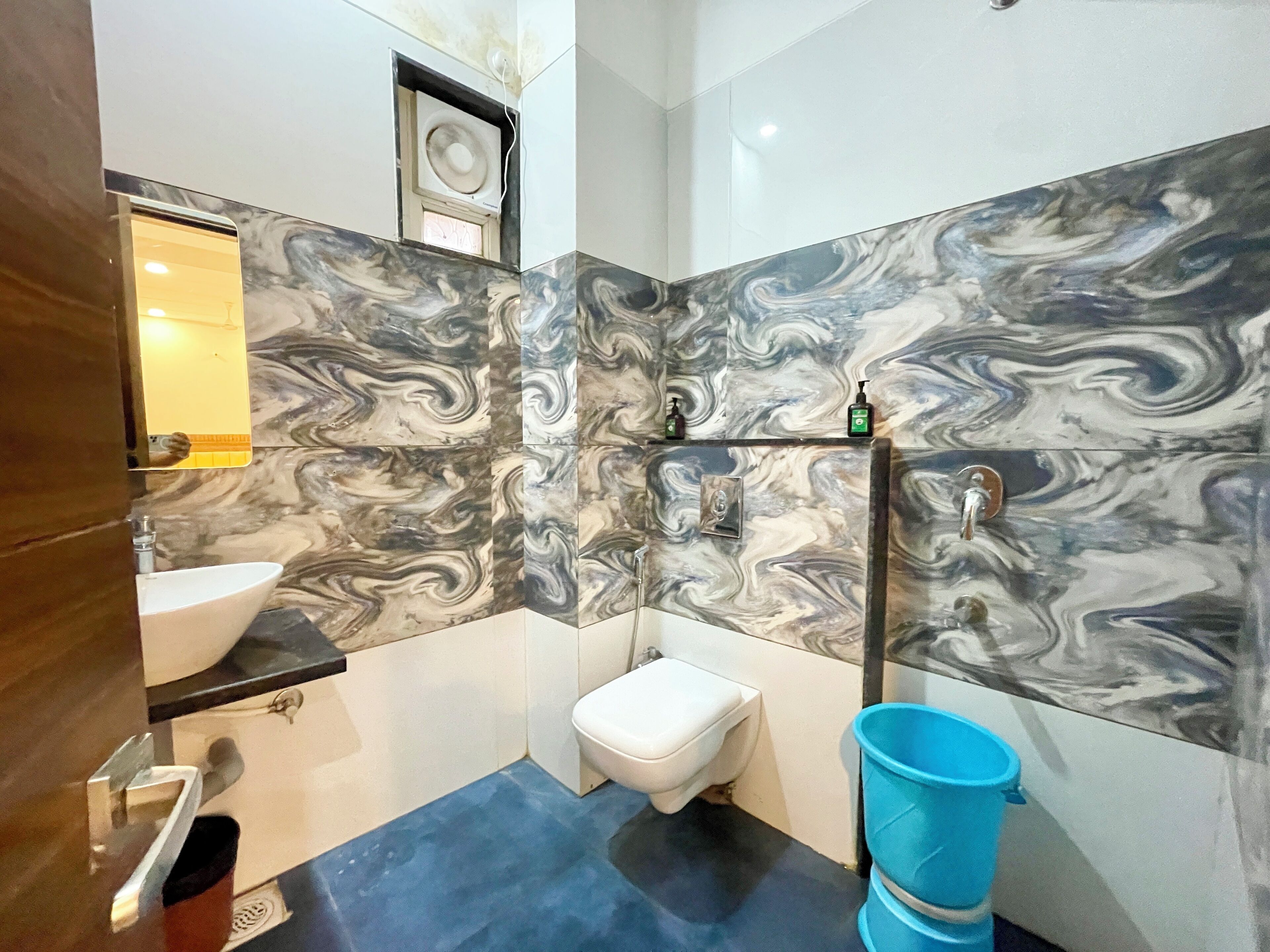 A bathroom with a marble backsplash, a white sink, a toilet, and a blue bucket.