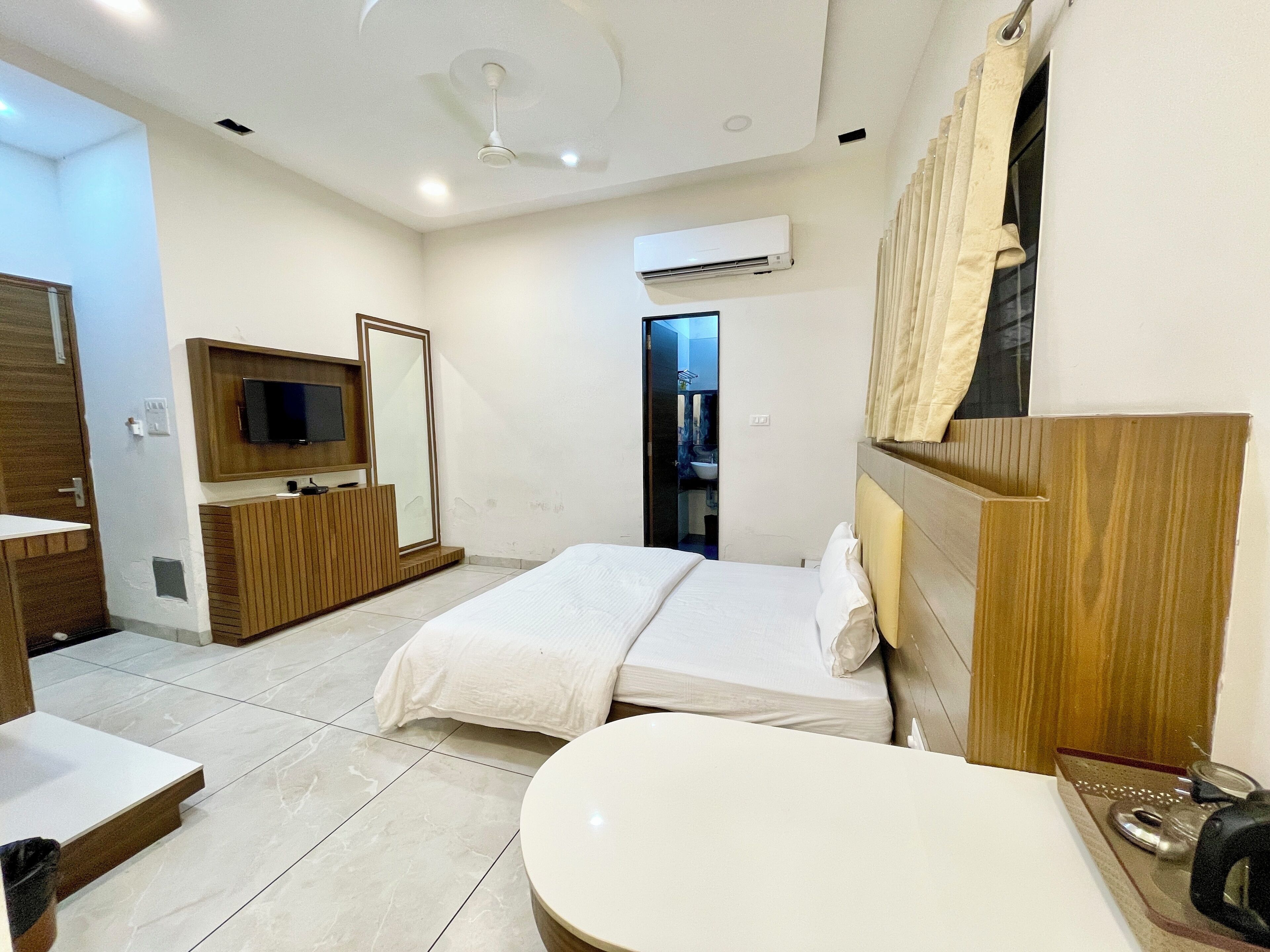 A hotel room with a bed, a TV mounted on the wall, a bathroom with a sink and mirror, and a ceiling fan.