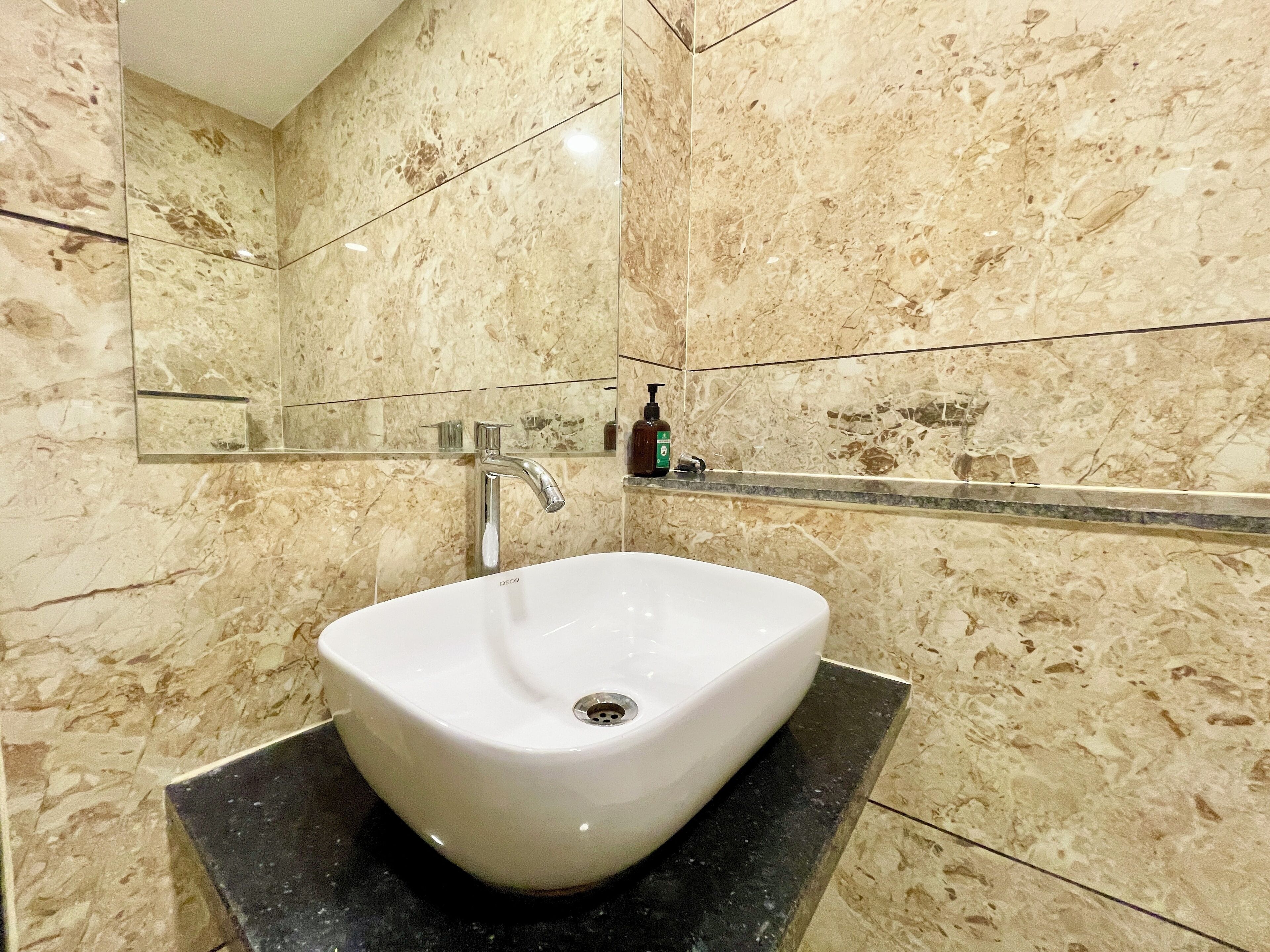 Une salle de bain avec un lavabo blanc, un miroir et un mur en marbre.