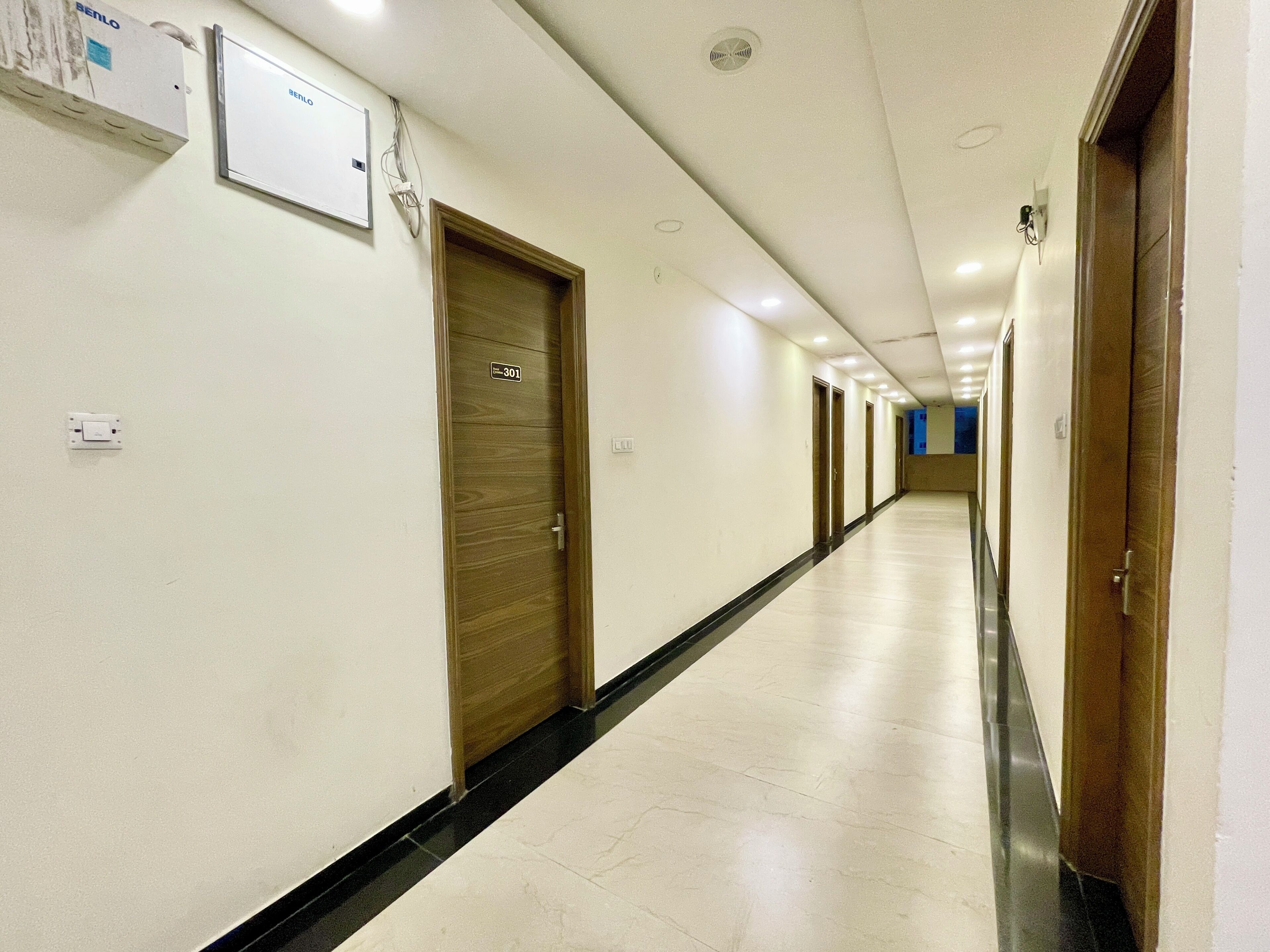 A long, narrow hotel corridor with wooden doors, a tiled floor, and a white wall with a sign above a door marked '301'.