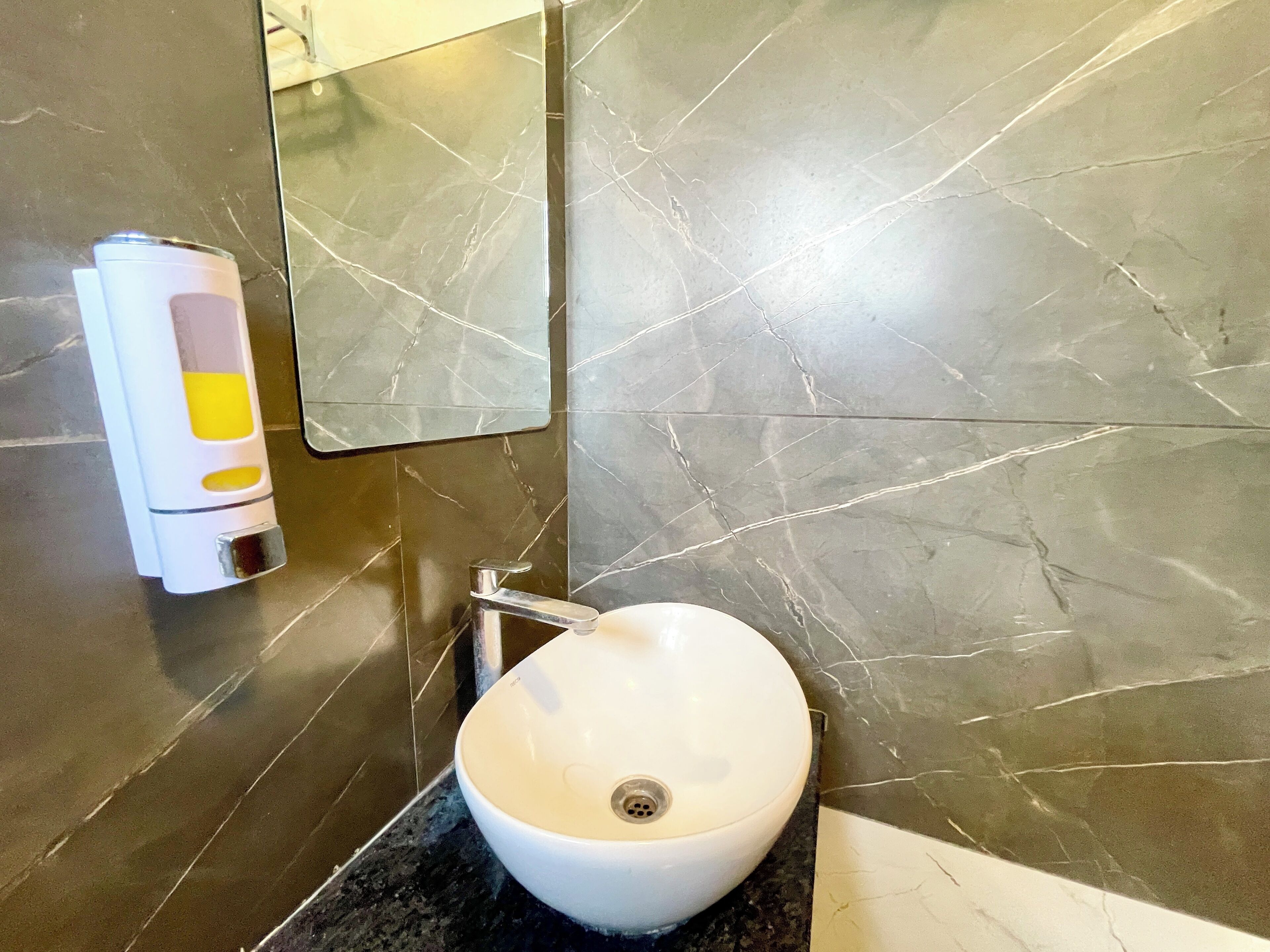 Une salle de bain avec un lavabo blanc, un robinet chromé et un distributeur de gel hydroalcoolique fixé au mur.
