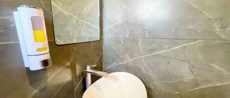 A bathroom with a white sink, a chrome faucet, and a hand sanitizer dispenser on the wall.