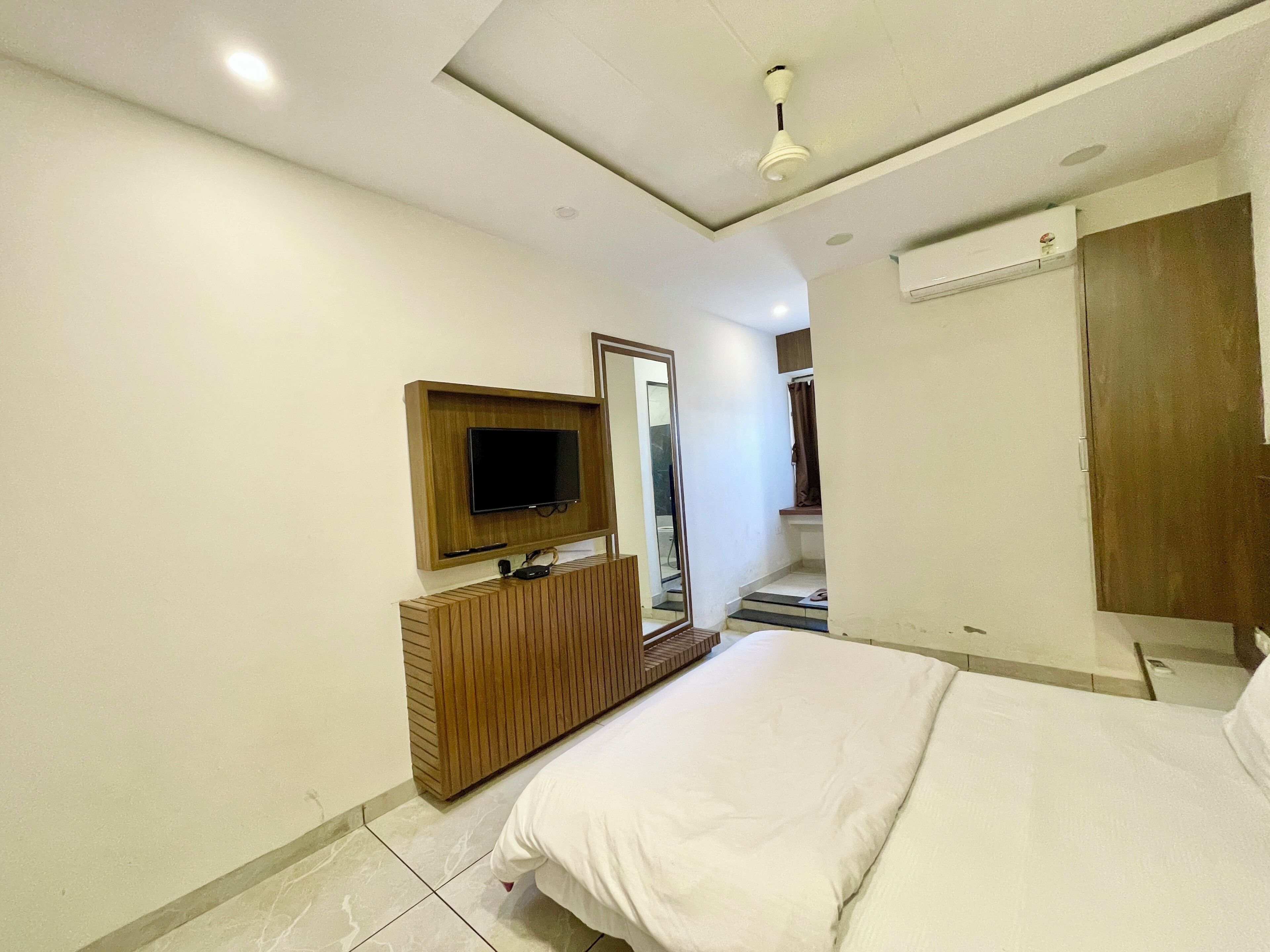 A modern hotel room with a bed, a TV mounted on the wall, a wooden dresser, and a mirror.
