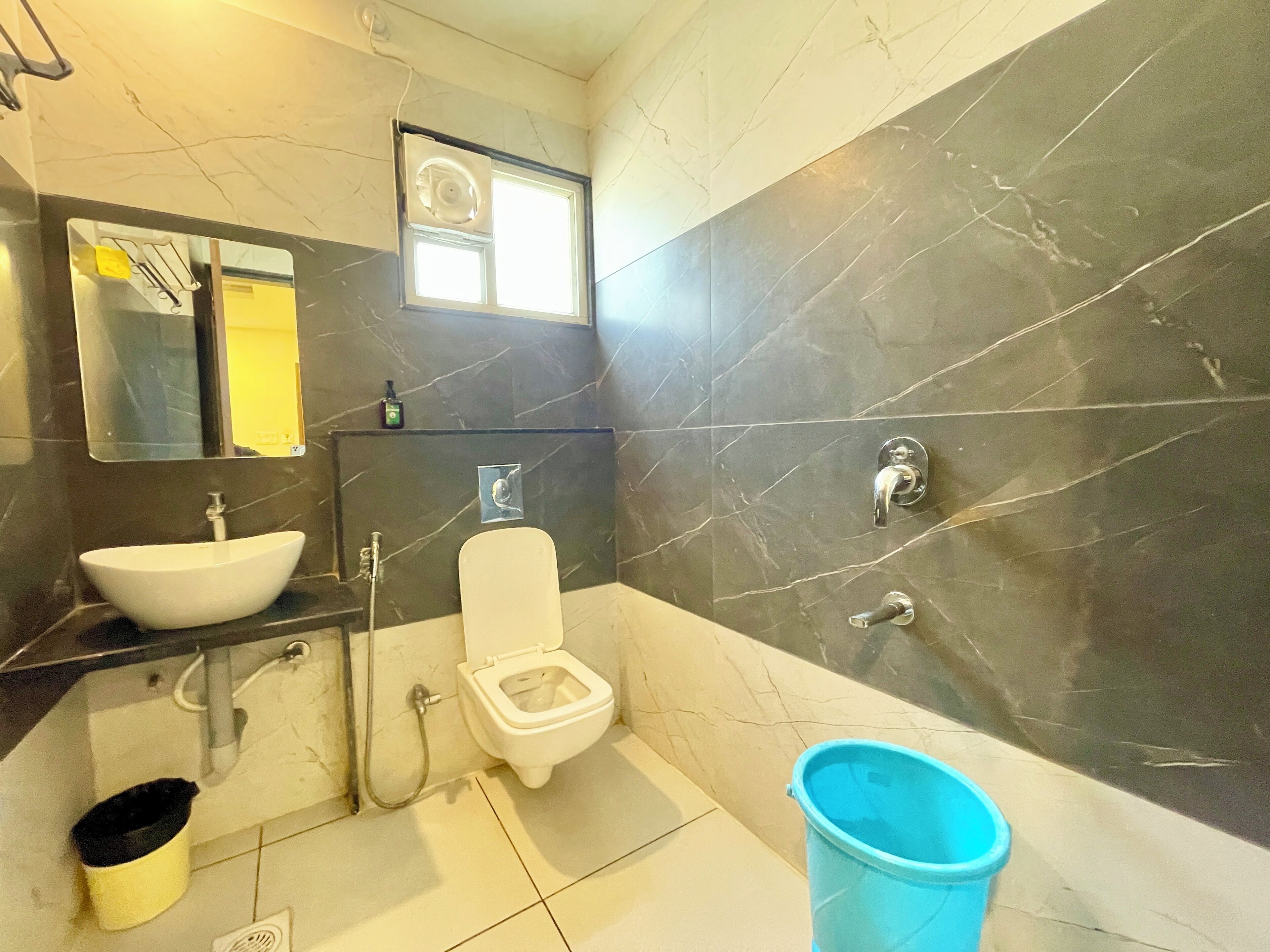 Ein Badezimmer mit Waschbecken, Toilette, blauem Eimer und Spiegel.