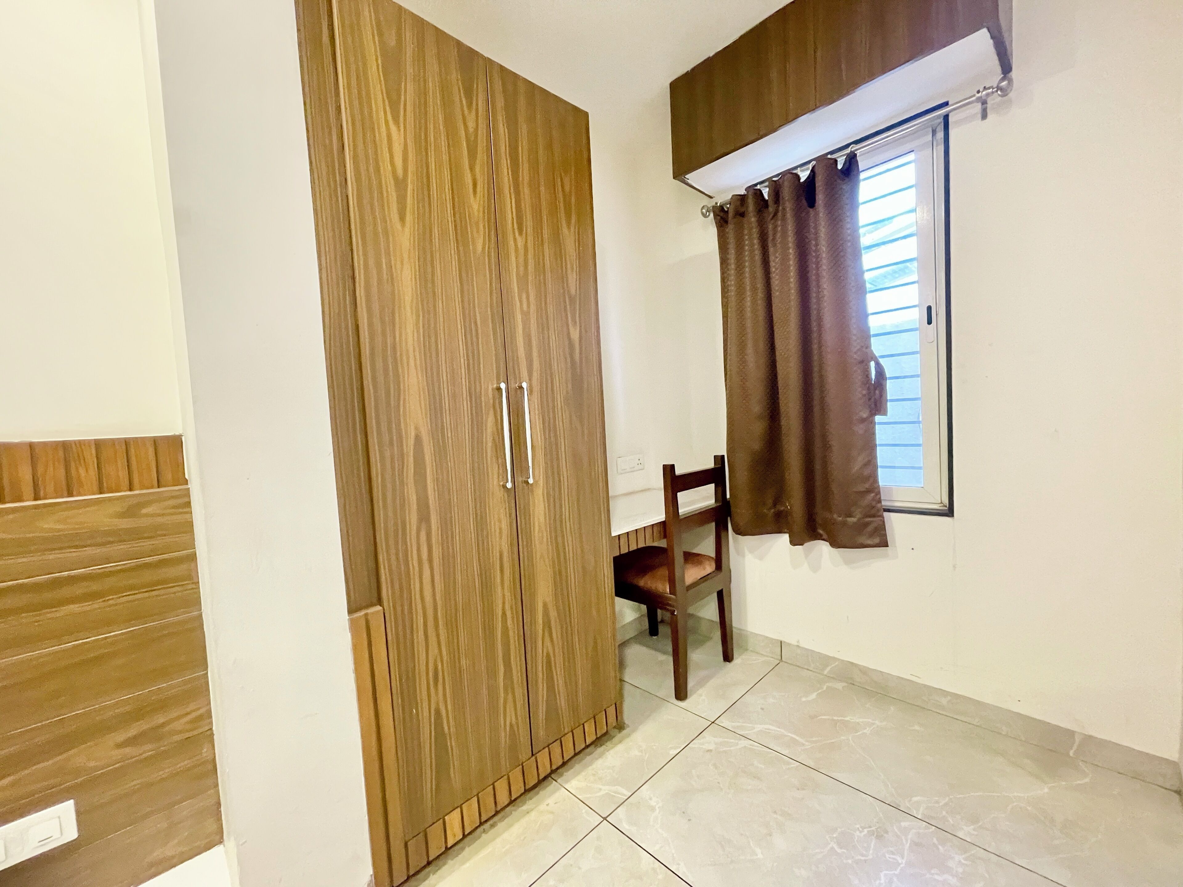 A room with a wooden wardrobe, a chair, and a window with curtains.