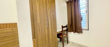 A room with a wooden wardrobe, a chair, and a window with curtains.