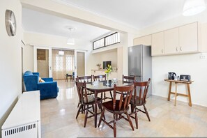 A modern kitchen with a dining area, featuring a round table, wooden chairs, and a built-in refrigerator. - Dragonfly Apartment in Chania (Chania)