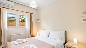 Une chambre à coucher comprenant un lit, deux tables de chevet, une commode, une fenêtre avec des rideaux et un climatiseur fixé au mur.