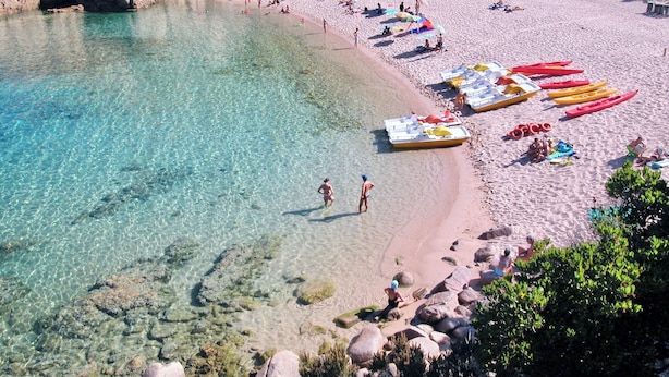 Ein Strand mit klarem Wasser, Kajaks und Menschen.