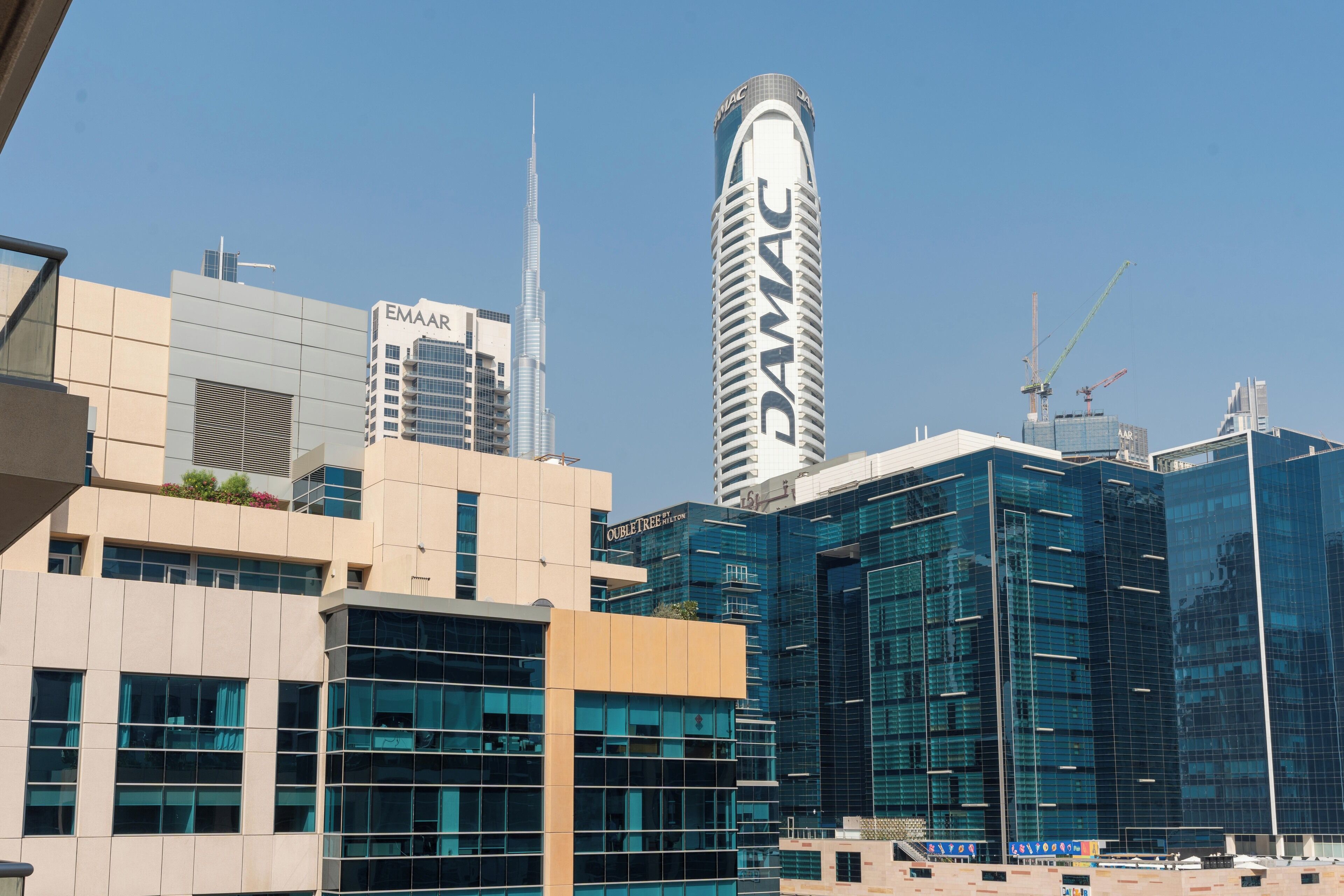 A modern urban skyline with prominent buildings including a tall cylindrical structure labeled "DAMAC".