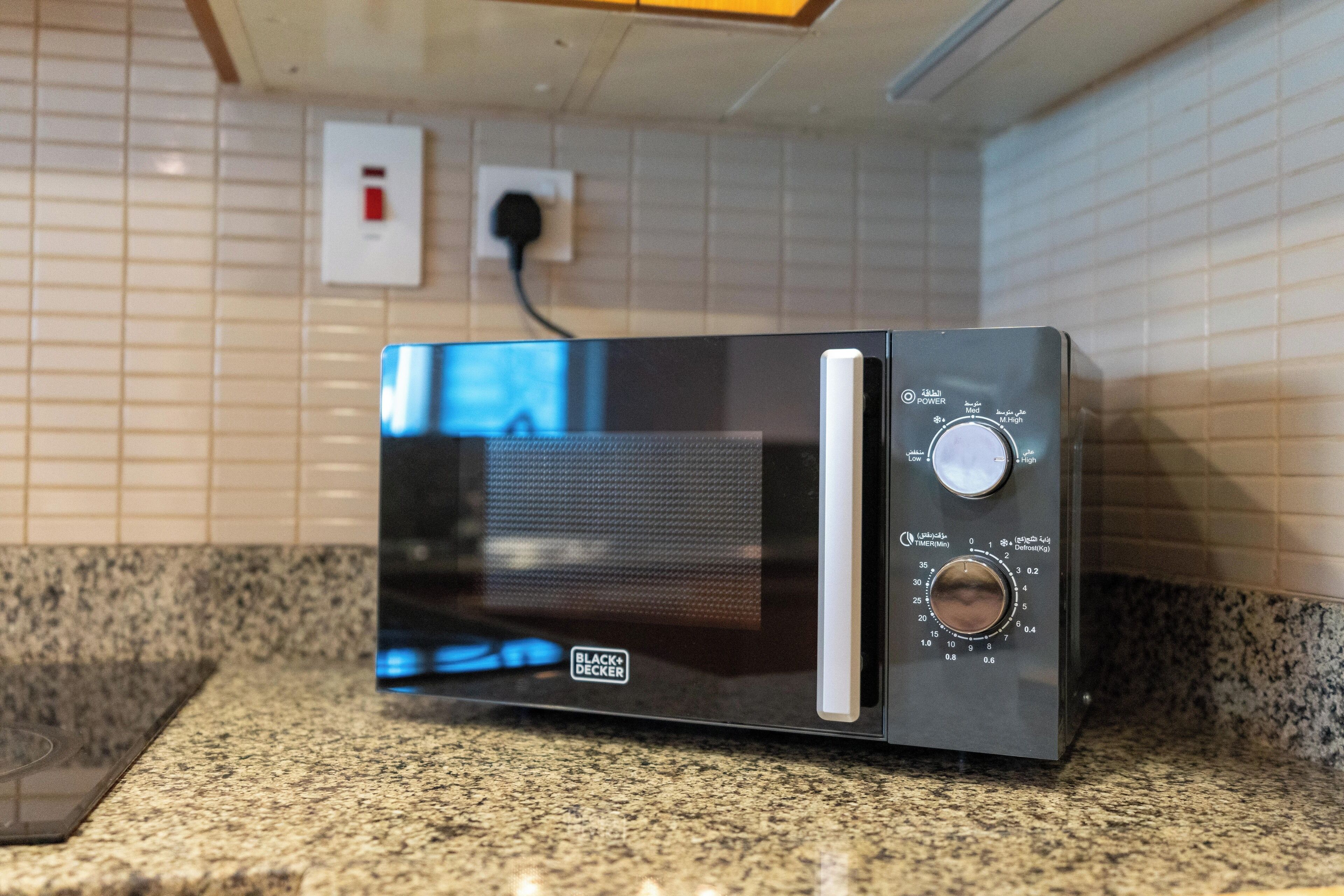 Um forno de micro-ondas sobre uma bancada de granito, com uma tomada e um interruptor na parede ao fundo.