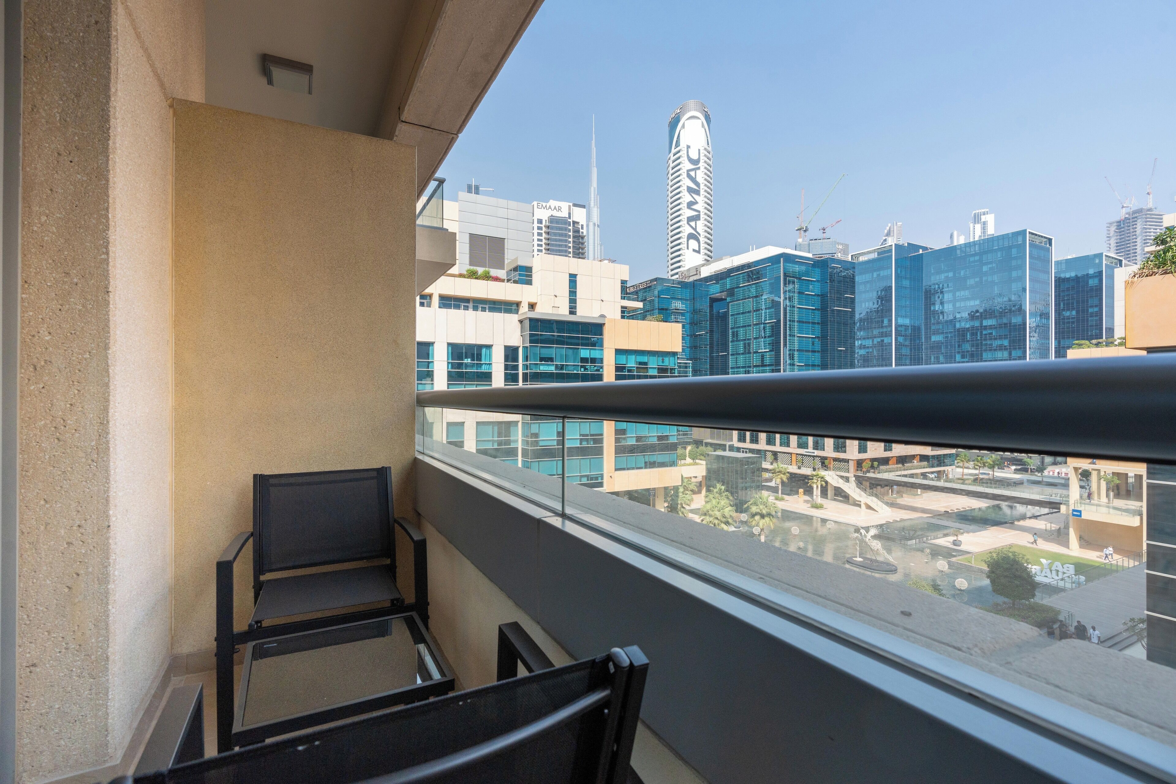 Ein Balkon mit zwei Stühlen und Blick auf moderne Gebäude, der Himmel ist klar.