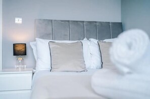 A neatly made bed with white and beige pillows, a grey headboard, and a bedside lamp with a black shade. - House 3 Bed Sleeps 6 -pets Ok -patio -free Parking (Manchester)