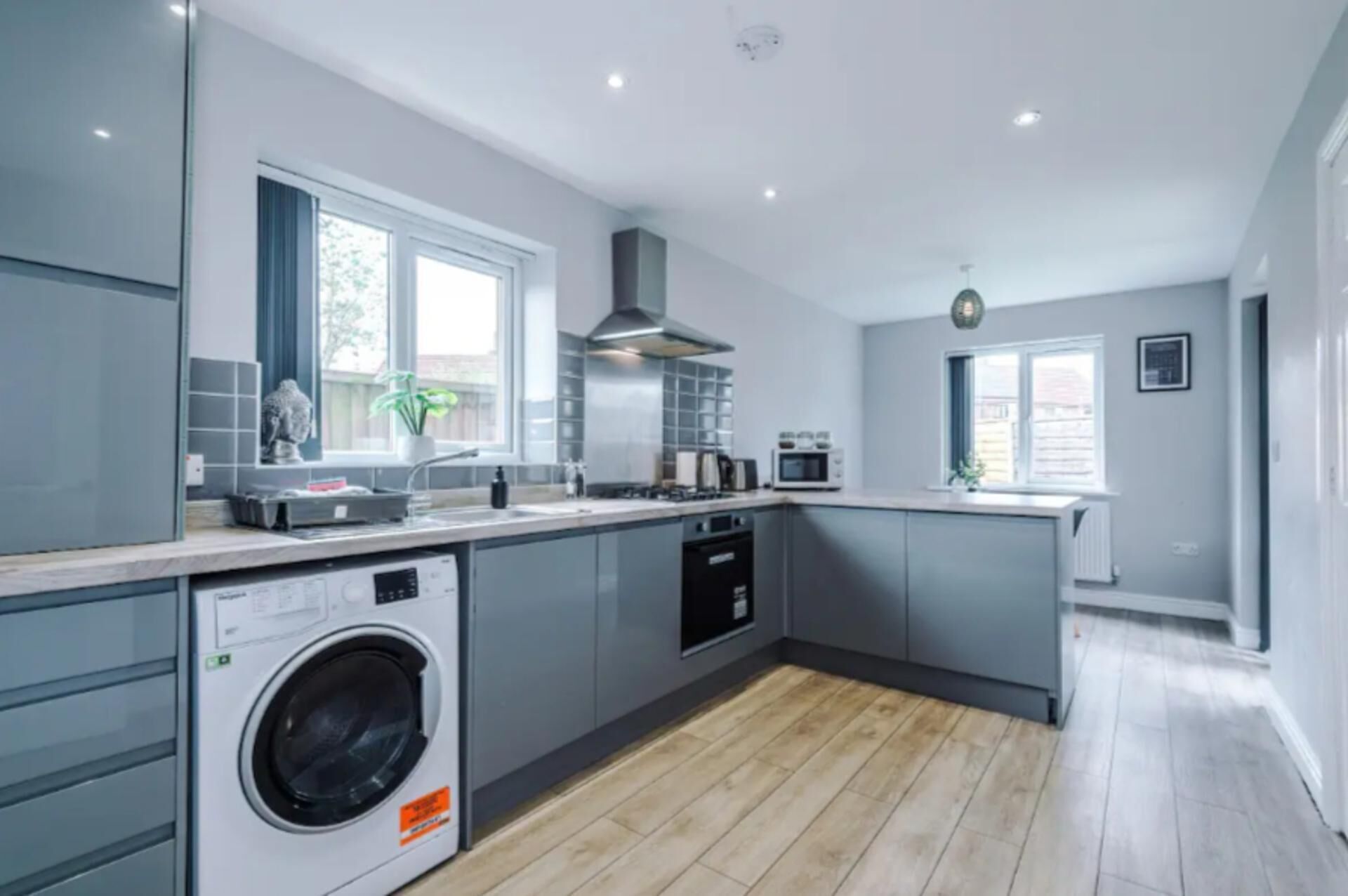 A modern kitchen with grey cabinetry, a built-in washing machine, a stove, and a microwave.