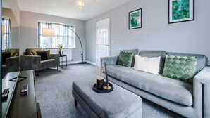 A modern living room with a grey sofa, two armchairs, a coffee table, and a floor lamp. There are two framed artworks on the wall and a window with blinds. - House 3 Bed Sleeps 6 -pets Ok -patio -free Parking (Manchester)