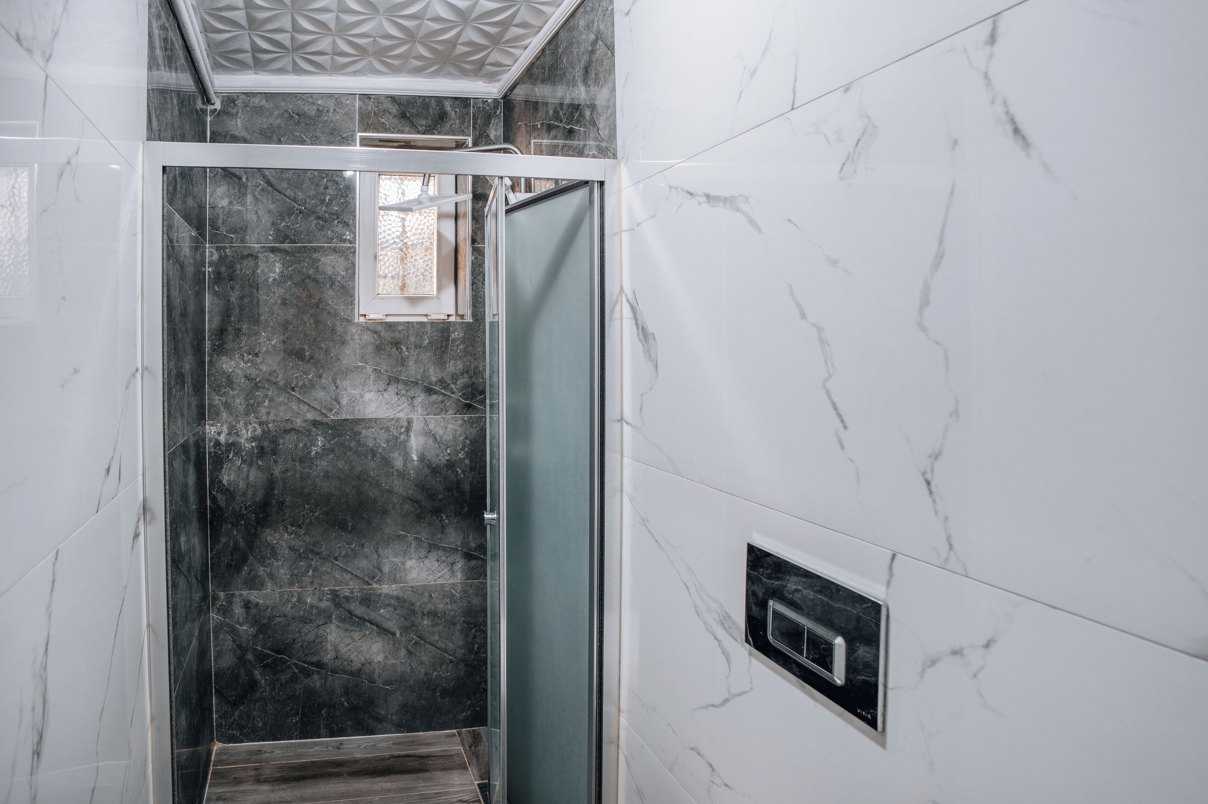 A modern bathroom with a glass shower enclosure, marble walls, and a built-in ventilation system.