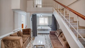 Un salon spacieux avec un plafond haut, un escalier et une chambre à coucher équipée d’un lit et de rideaux.