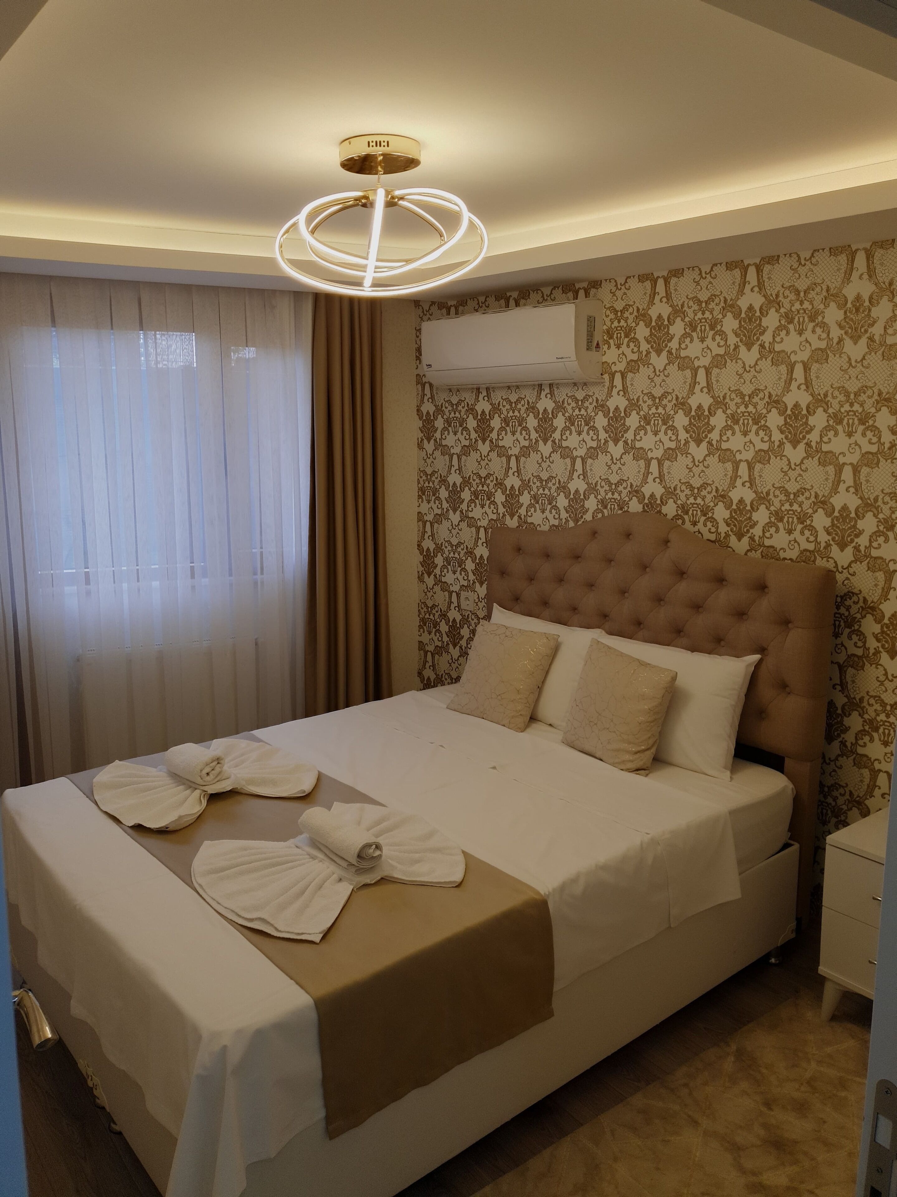 A neatly made bed with a tufted headboard, a bedside table, and a wall-mounted air conditioner.