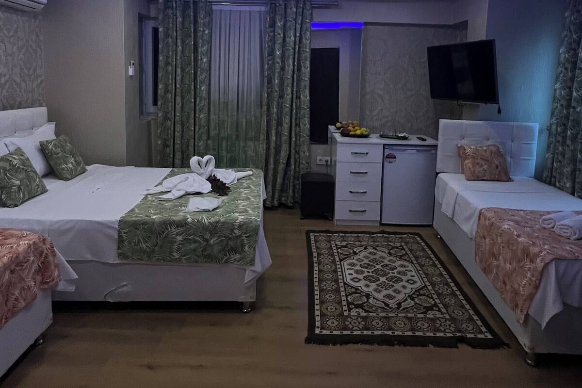 A modern hotel room with two beds, a flat-screen TV, a desk, and a large window with curtains.