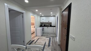 Un couloir étroit qui donne sur un coin cuisine, un coin repas et une chambre, cette dernière étant visible à travers une porte ouverte.