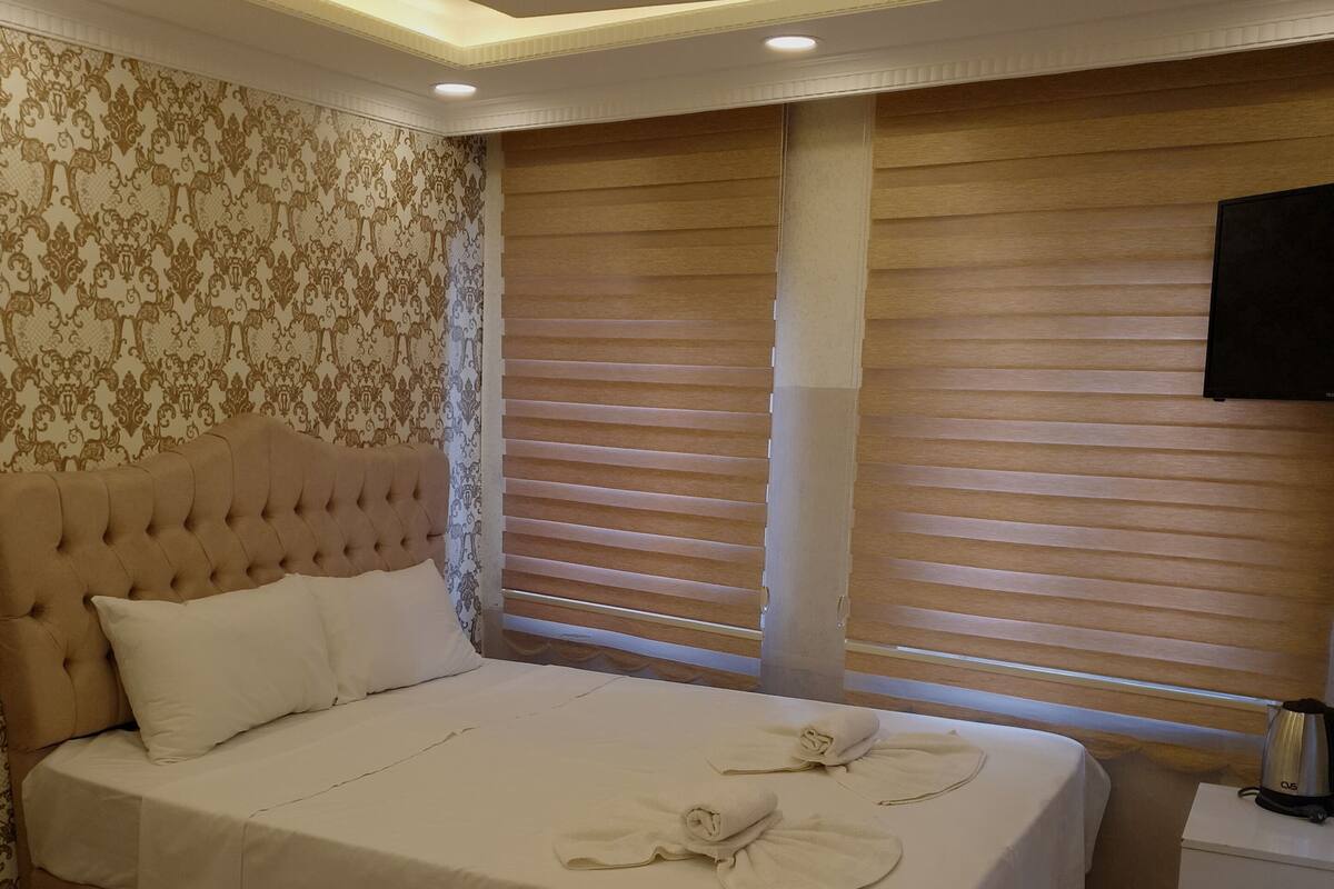 A hotel room with two beds, a wooden headboard, a patterned wallpaper, a wooden floor, and a flat-screen TV.