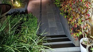 Un estrecho sendero empedrado que lleva a una escalera rodeada de abundante vegetación y un muro rústico.