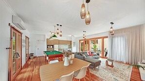 Amplia sala de estar con mesa de billar, mesa de comedor con sillas, sofá y un ventanal con cortinas.