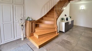 A wooden staircase with a handrail, leading to an upper floor. There is a white cabinet with a vase of dried plants on the landing.