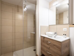 Une salle de bain moderne avec une douche à parois de verre, un meuble-lavabo en bois avec un vasque blanche et un grand miroir.