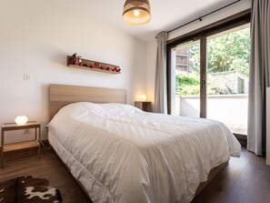 Une chambre avec un grand lit, une table de chevet avec une lampe, une étagère avec des objets décoratifs et une vue sur l’extérieur par une fenêtre.
