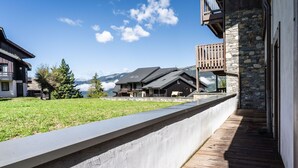 Un bâtiment moderne avec une façade en pierre, une terrasse en bois et une vue sur les montagnes en arrière-plan.