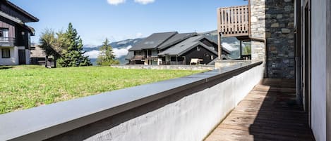 A modern building with a stone facade, a wooden deck, and a view of mountains in the background.