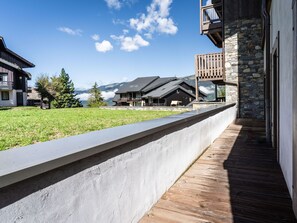 A modern building with a stone facade, a wooden deck, and a view of mountains in the background. - Cozy apartment in resort center, near slopes, parking, WiFi (La Plagne Montalbert)