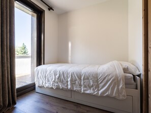 A bedroom with a bed, a window with curtains, and a view of the outdoors. - Cozy apartment in resort center, near slopes, parking, WiFi (La Plagne Montalbert)