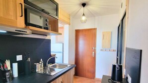 Una cocina compacta con armarios de madera, una encimera negra, un lavabo de acero inoxidable, un microondas y una cafetera negra.