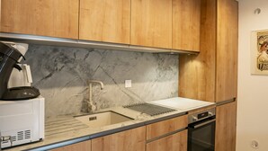 Una cocina moderna con armarios de madera, salpicadero de mármol, pileta de acero inoxidable y horno empotrado.