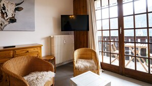 Una habitación acogedora con muebles de mimbre, un televisor y un ventanal con vistas a una terraza de madera y montañas.