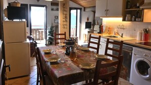 Un comedor con una mesa dispuesta para cuatro personas, un refrigerador, una lavadora y una encimera de cocina con diversos objetos.