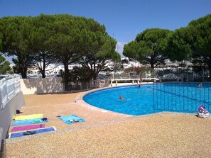 Piscina com área de praia de pedras, cercada por árvores e um muro.
