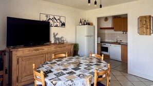 Een kleine keuken met een eethoek, een televisie en een klok aan de muur.