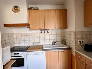 A compact kitchen with wooden cabinets, a microwave, an oven, a dishwasher, and a sink.