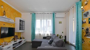 Moderni olohuone, jossa on litteänäyttöinen televisio, sohva ja valkoinen kaappi, sekä ruokailutila.
