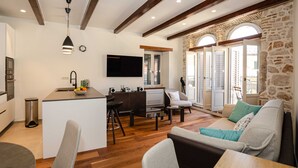 A modern kitchen with a central island, a dining area with a sofa and chairs, and a stone wall with a circular window. - Luxury and Timeless Haven Apartment Rovinj (Rovinj)