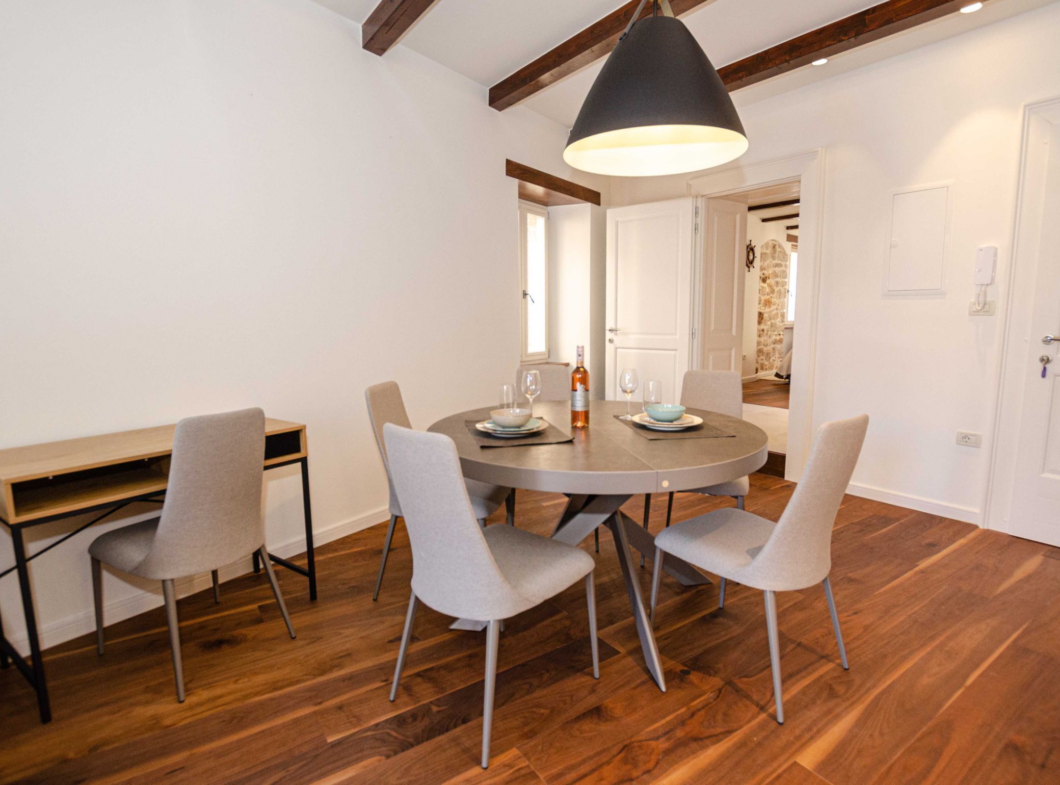 Zona pranzo con tavolo rotondo, quattro sedie, lampadario e pavimento in legno.