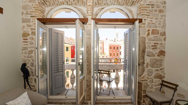 A room with a stone wall, a wooden ceiling, and a balcony with a view of buildings. - Luxury and Timeless Haven Apartment Rovinj (Rovinj)