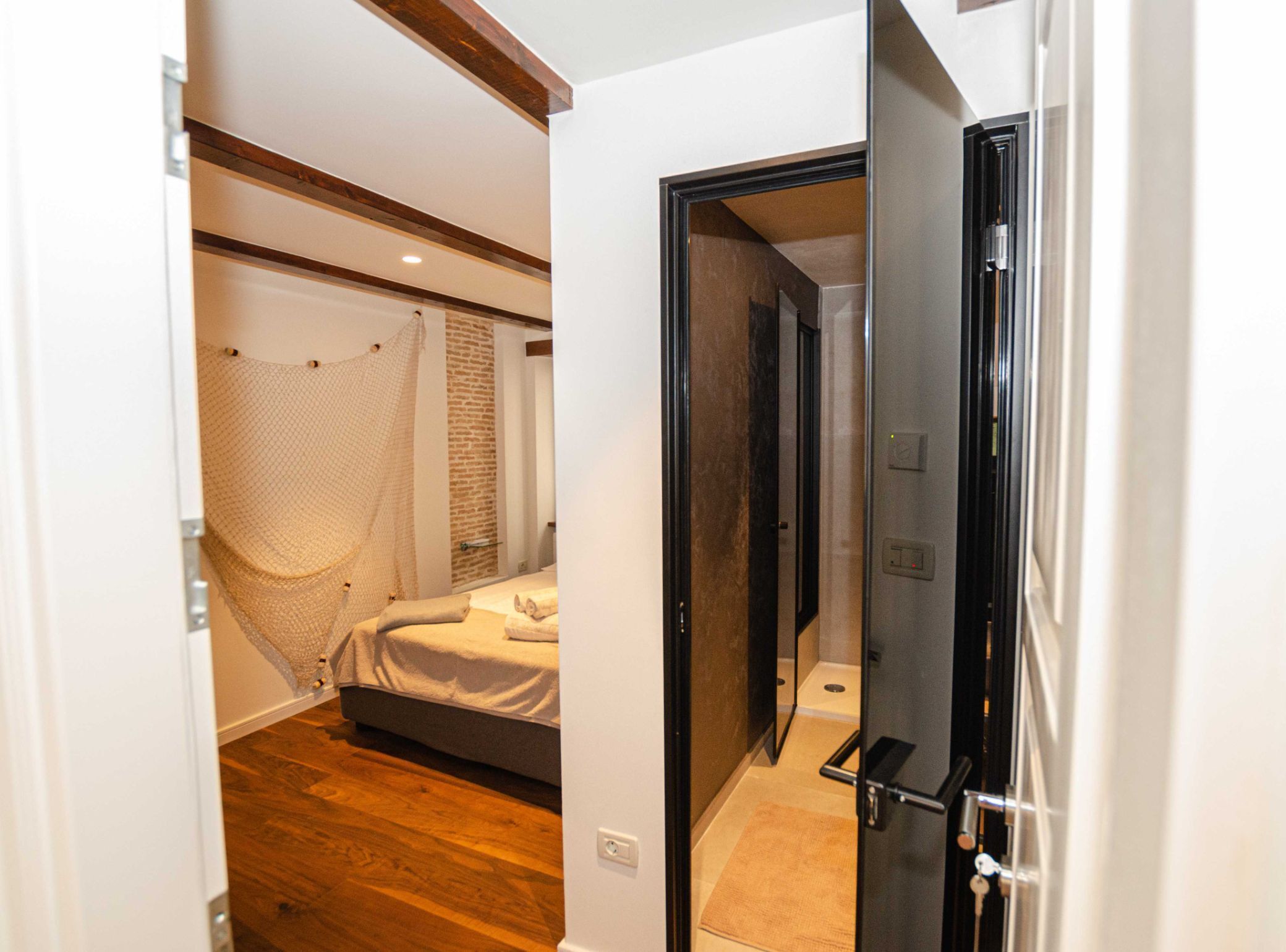 Ein Schlafzimmer mit einem Bett, Holzboden, Backsteinwand und einer Tür zu einem anderen Raum.