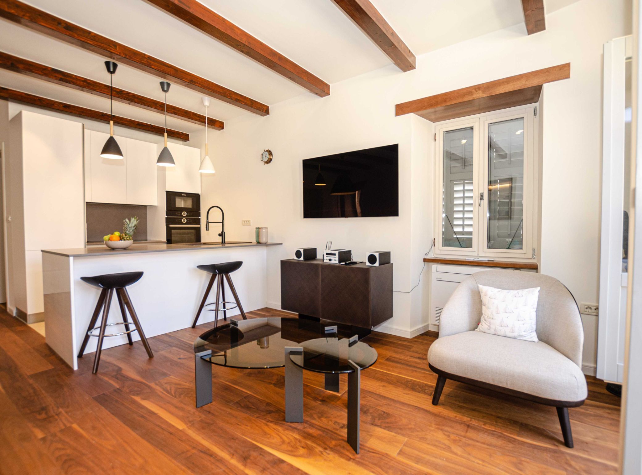 A modern kitchen with a central island, bar stools, a dining table, and a sofa.