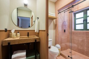 Ein Badezimmer mit rundem Spiegel, Waschbecken mit Seifenspender, Toilette und einer Duschkabine.
